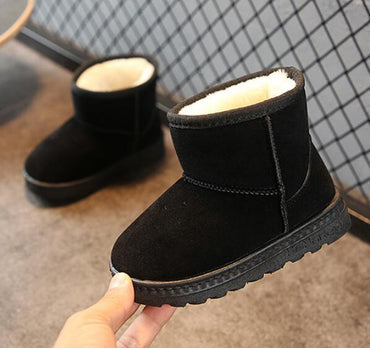 Black snow boots with white fur lining held by a hand on a checkered floor background